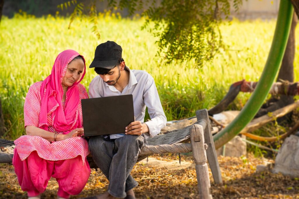 Outdoor portrait of Indian teenager grandson helping rural senior grandmother how to use a laptop.
